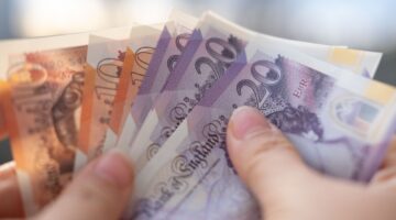 Person holding various British banknotes in different denominations.