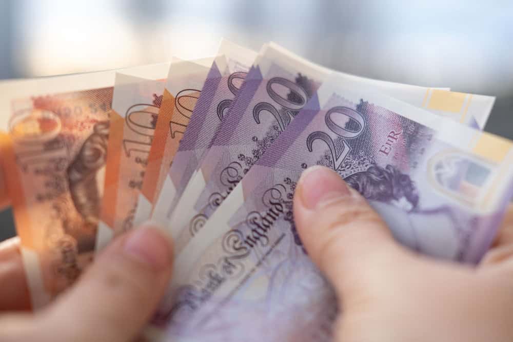 Person holding various British banknotes in different denominations.