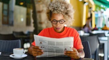 A woman reading a newspaper in a café.
