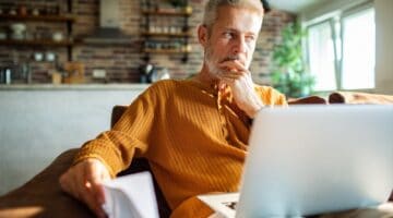 A man in his 50s thinking while using a laptop