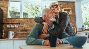 An older couple smiling and hugging at the dinner table.