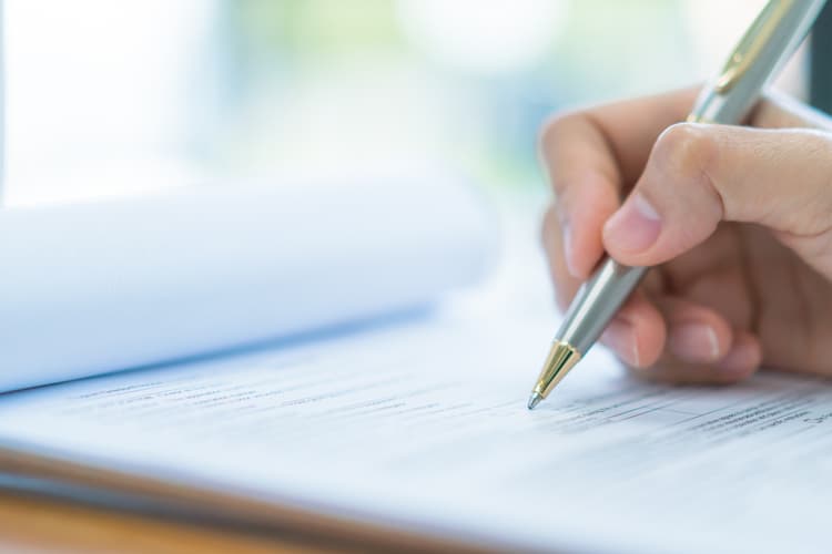 A hand holding a pen and marking paperwork.