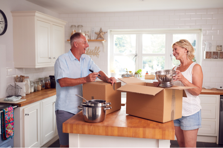 A couple packing items into a box in a kitchen.