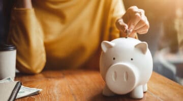 A woman placing a coin in a piggy bank.