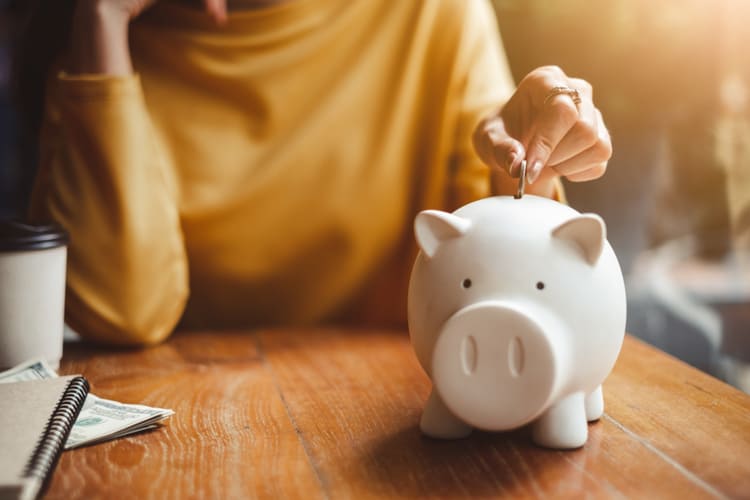A woman placing a coin in a piggy bank.