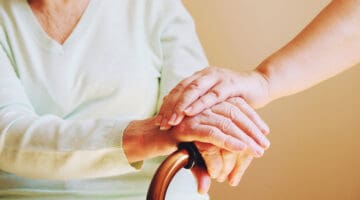 Close-up of someone holding hand the hand of an older woman with a walking aid.