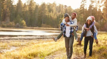Parents walking through a park giving children a piggyback ride.