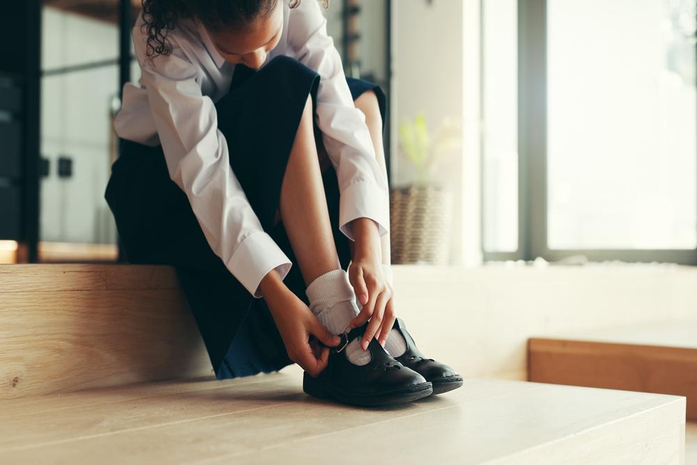 A girl putting on school shoes.