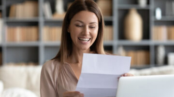 A woman smiling as she reads a letter.